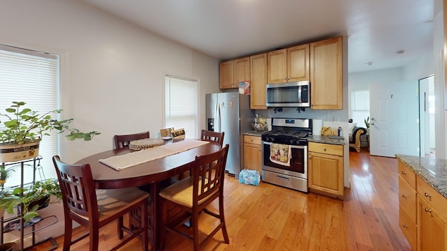 kitchen with light brown cabinets, light stone counters, light hardwood / wood-style floors, and stainless steel appliances