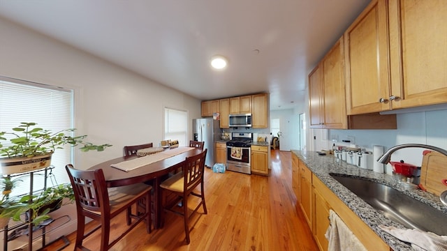 kitchen featuring stainless steel appliances, sink, a wealth of natural light, stone counters, and light hardwood / wood-style flooring