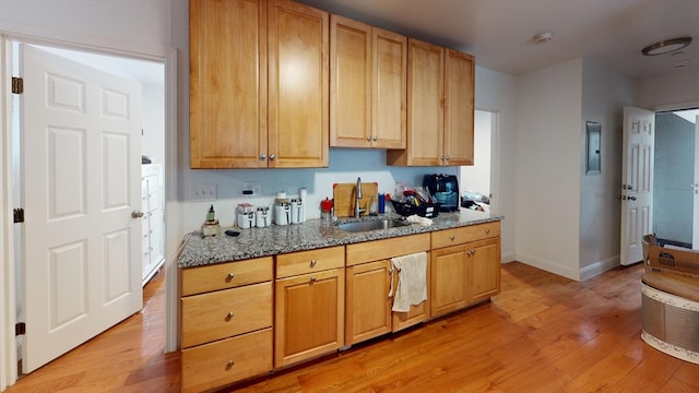 kitchen with dark stone countertops, sink, and light hardwood / wood-style flooring