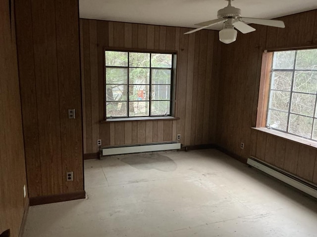 empty room with a baseboard heating unit, plenty of natural light, and wooden walls