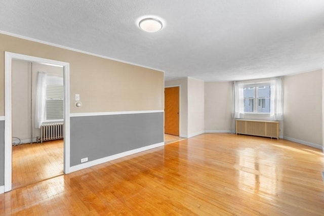 spare room featuring crown molding, radiator heating unit, and light wood-type flooring