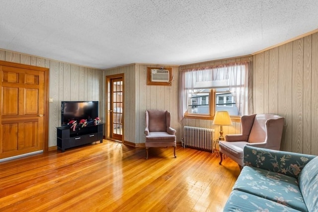 sitting room with radiator, light hardwood / wood-style floors, a wall unit AC, and a textured ceiling