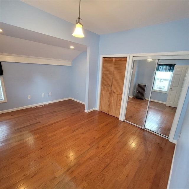 unfurnished bedroom with hardwood / wood-style flooring, radiator, and multiple closets