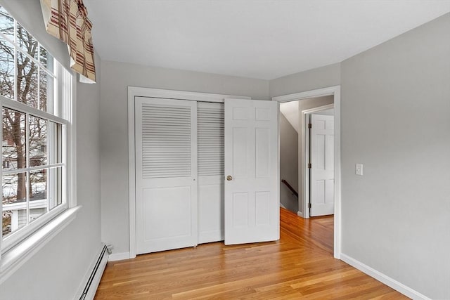 unfurnished bedroom featuring a baseboard heating unit, light hardwood / wood-style floors, and a closet