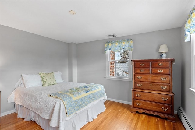 bedroom with multiple windows, a baseboard heating unit, and light hardwood / wood-style floors