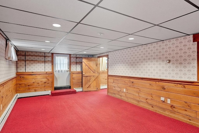 basement with wood walls, a baseboard radiator, a barn door, and carpet flooring