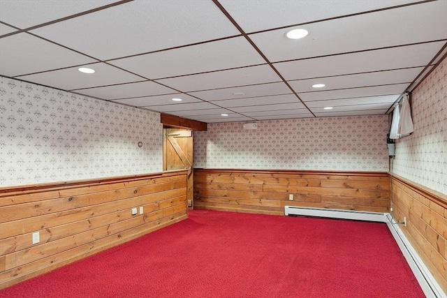 basement with baseboard heating, a paneled ceiling, carpet, and wood walls