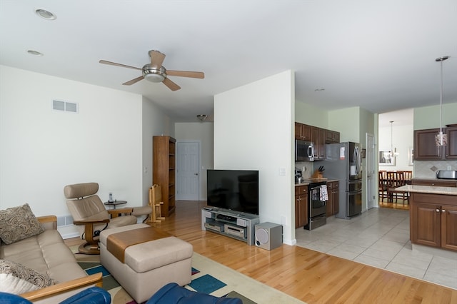 living room with ceiling fan with notable chandelier and light wood-type flooring