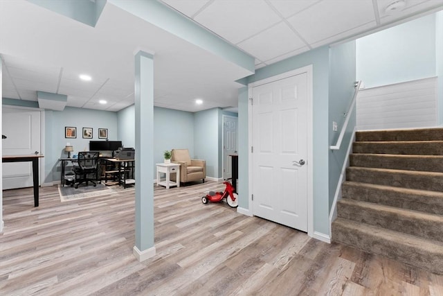 finished below grade area with light wood-type flooring, stairs, a paneled ceiling, and baseboards