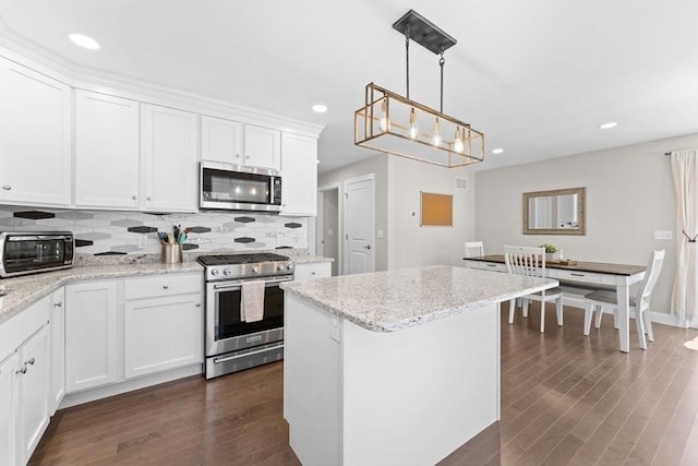 kitchen with a kitchen island, backsplash, dark wood finished floors, white cabinets, and stainless steel appliances
