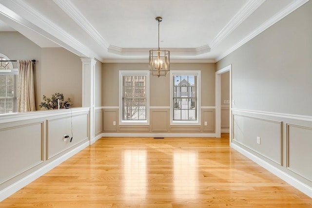 unfurnished dining area with a chandelier, light wood-type flooring, ornamental molding, a tray ceiling, and decorative columns