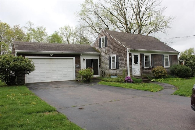 new england style home featuring asphalt driveway, an attached garage, a shingled roof, and a front lawn