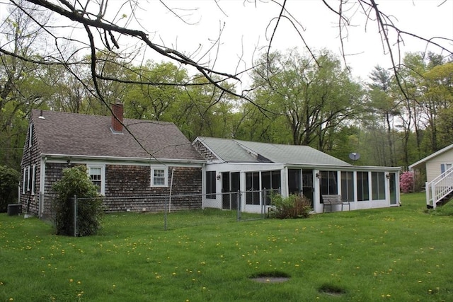 rear view of house featuring a sunroom, a lawn, a chimney, and cooling unit