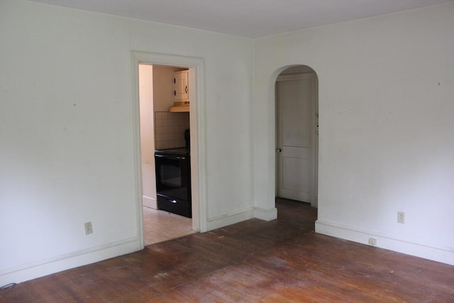 unfurnished room featuring wood finished floors, arched walkways, and baseboards