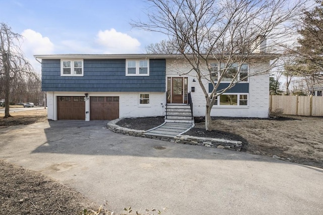 bi-level home with brick siding, aphalt driveway, fence, and a garage