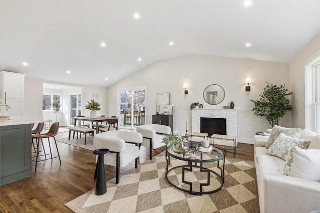 living room featuring lofted ceiling, a brick fireplace, recessed lighting, and wood finished floors