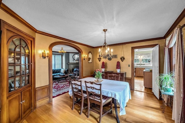 68 Ingersoll Grv, Springfield, MA 01109 - dining room featuring wainscoting, light wood-style floors, a textured ceiling, a chandelier, and arched walkways