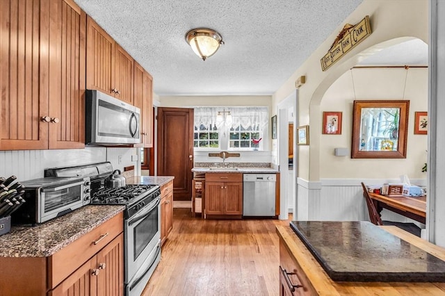 68 Ingersoll Grv, Springfield, MA 01109 - kitchen featuring a textured ceiling, a wainscoted wall, arched walkways, light wood finished floors, and stainless steel appliances