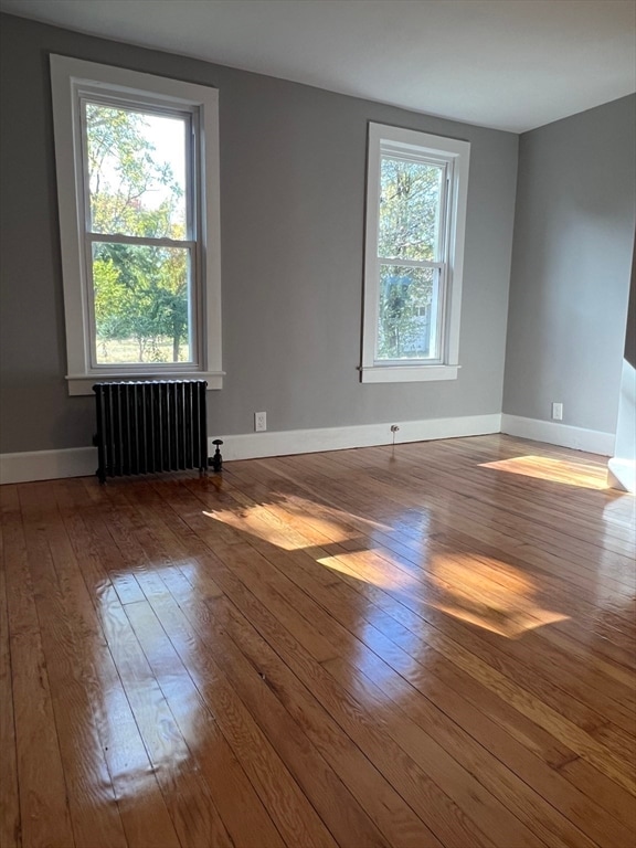 empty room featuring hardwood / wood-style flooring, a wealth of natural light, and radiator