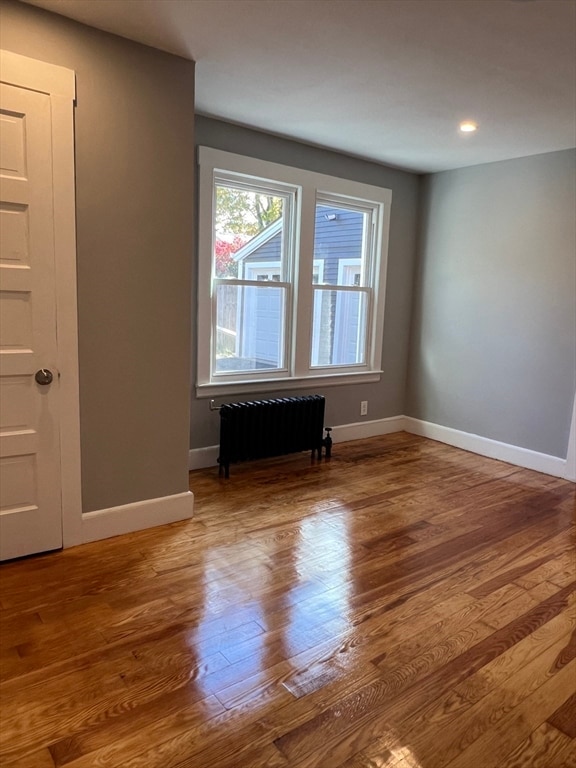 empty room with radiator heating unit and hardwood / wood-style flooring