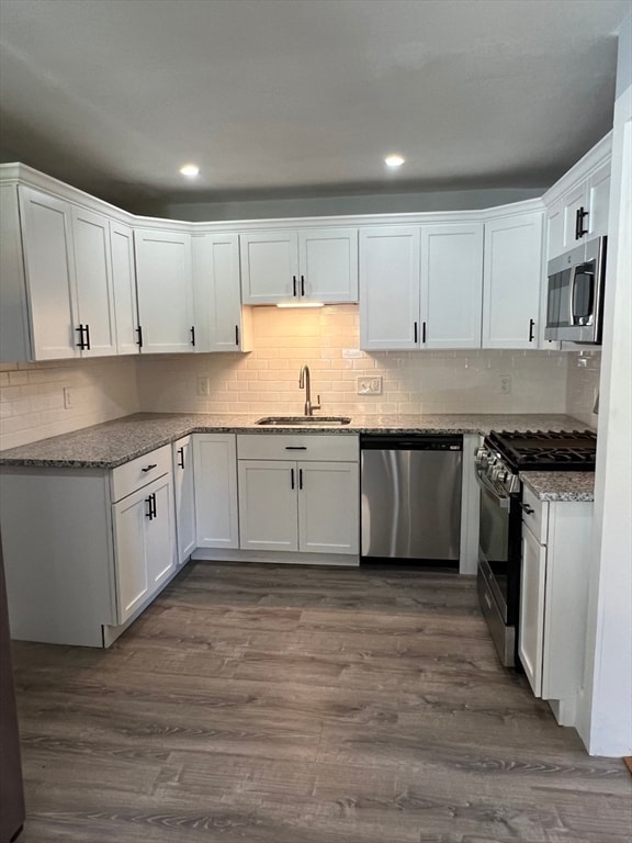 kitchen with appliances with stainless steel finishes, dark hardwood / wood-style flooring, sink, stone counters, and white cabinetry