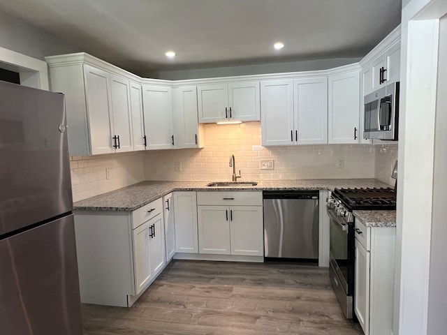 kitchen with light stone counters, stainless steel appliances, sink, light hardwood / wood-style floors, and white cabinetry