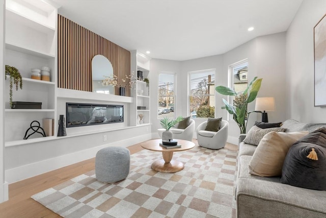 living room featuring baseboards, wood finished floors, recessed lighting, built in features, and a glass covered fireplace