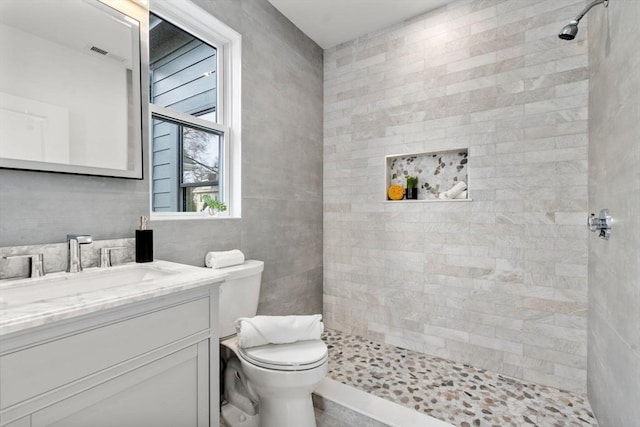full bathroom featuring toilet, vanity, a tile shower, and visible vents