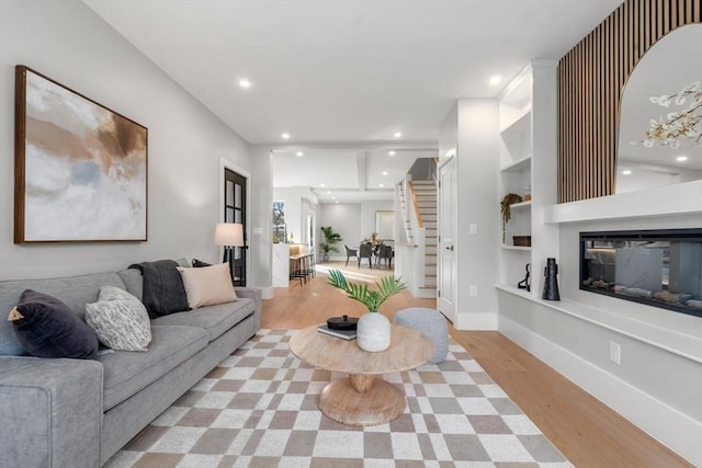 living room with recessed lighting, light wood-type flooring, baseboards, built in shelves, and a glass covered fireplace