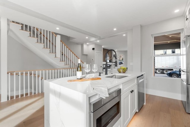 kitchen with a sink, light wood finished floors, light stone countertops, appliances with stainless steel finishes, and a kitchen island with sink