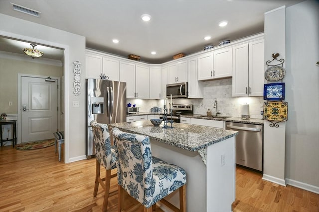 kitchen with a kitchen breakfast bar, sink, appliances with stainless steel finishes, stone countertops, and white cabinetry