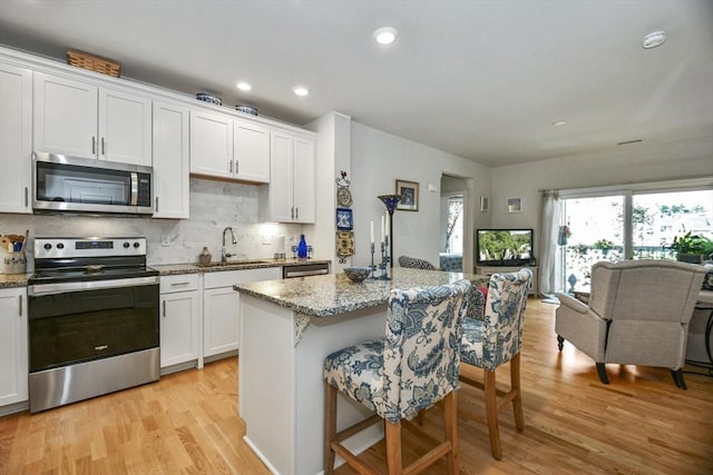 kitchen with a kitchen bar, appliances with stainless steel finishes, light stone counters, sink, and white cabinetry