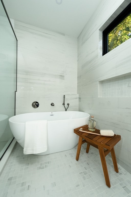 bathroom with a tub to relax in and tile walls