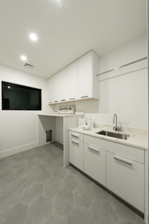 clothes washing area with cabinets, light tile patterned floors, and sink