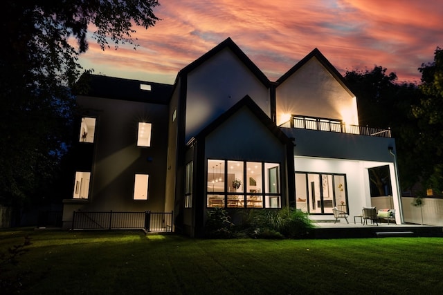 back house at dusk with a balcony, a patio area, and a yard