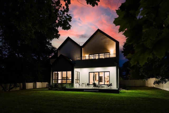 back house at dusk with a lawn, a balcony, and a patio area