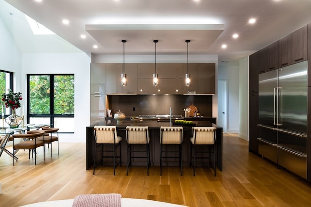 kitchen featuring light hardwood / wood-style floors, built in refrigerator, tasteful backsplash, and a breakfast bar area