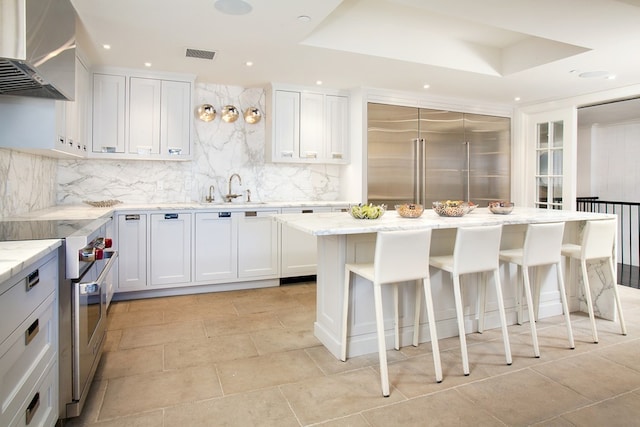 kitchen with tasteful backsplash, a raised ceiling, visible vents, wall chimney range hood, and premium appliances