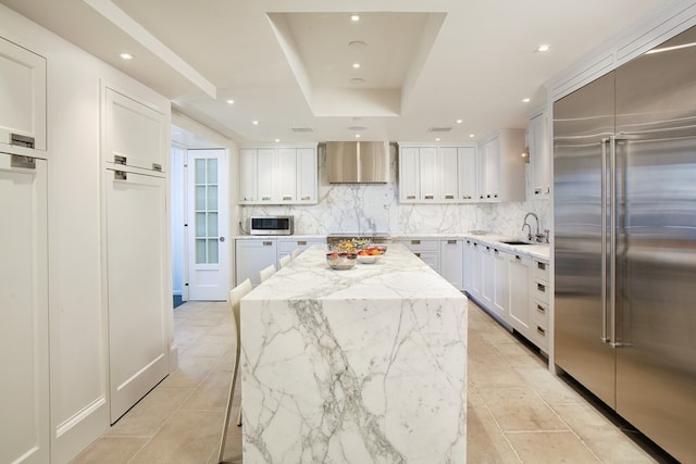 kitchen featuring a tray ceiling, decorative backsplash, a kitchen island, a sink, and appliances with stainless steel finishes