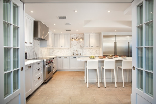 kitchen featuring sink, premium appliances, wall chimney range hood, white cabinetry, and a breakfast bar