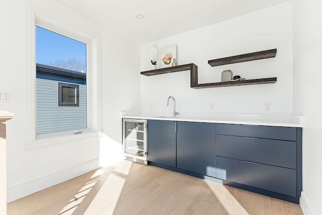 bar featuring blue cabinetry, sink, beverage cooler, and light hardwood / wood-style floors