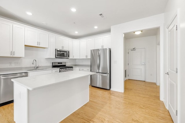 kitchen with white cabinets, sink, light hardwood / wood-style flooring, appliances with stainless steel finishes, and a kitchen island