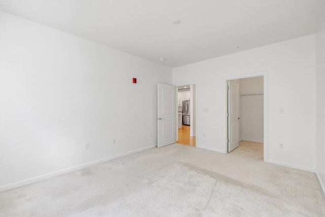 unfurnished bedroom featuring a walk in closet, light carpet, stainless steel refrigerator, and a closet