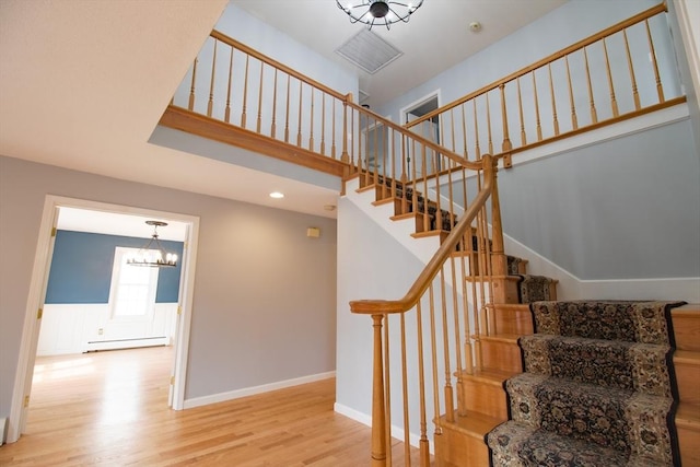 stairs featuring a baseboard heating unit, baseboards, a chandelier, a high ceiling, and wood finished floors