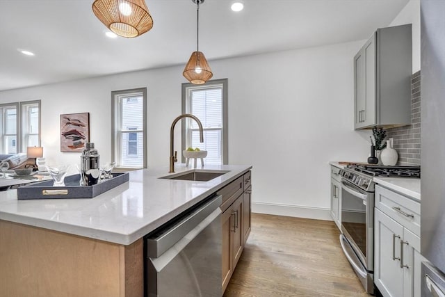 kitchen featuring a kitchen island with sink, sink, decorative light fixtures, light stone counters, and stainless steel appliances