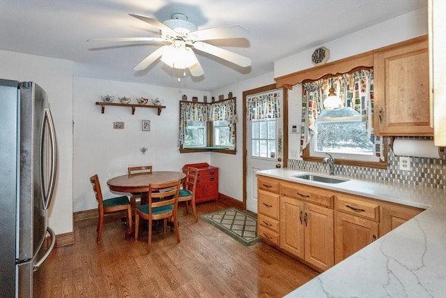 kitchen featuring light stone counters, a sink, light wood-style floors, freestanding refrigerator, and decorative backsplash