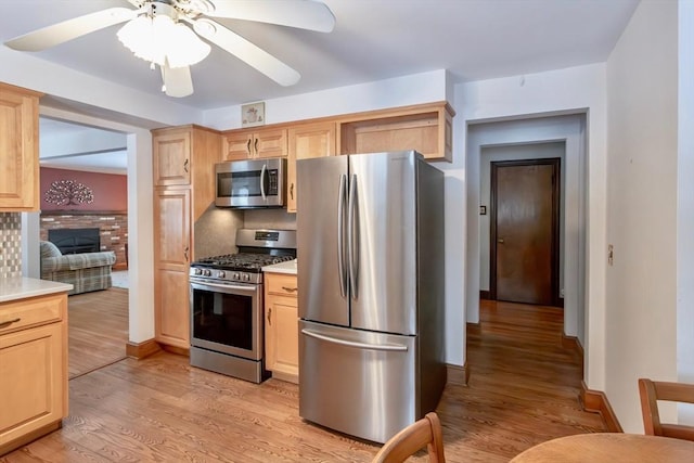 kitchen featuring a fireplace, light countertops, appliances with stainless steel finishes, light wood-style floors, and light brown cabinets