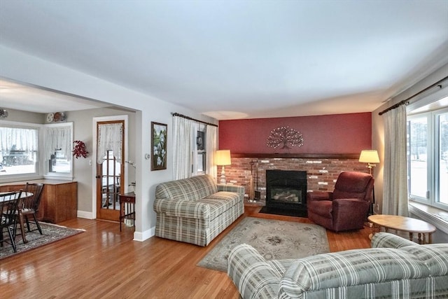 living room featuring a brick fireplace, baseboards, and wood finished floors