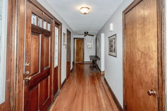 hall with a textured ceiling, baseboards, and wood finished floors