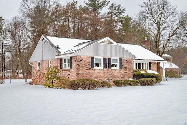 snow covered property with brick siding and a chimney